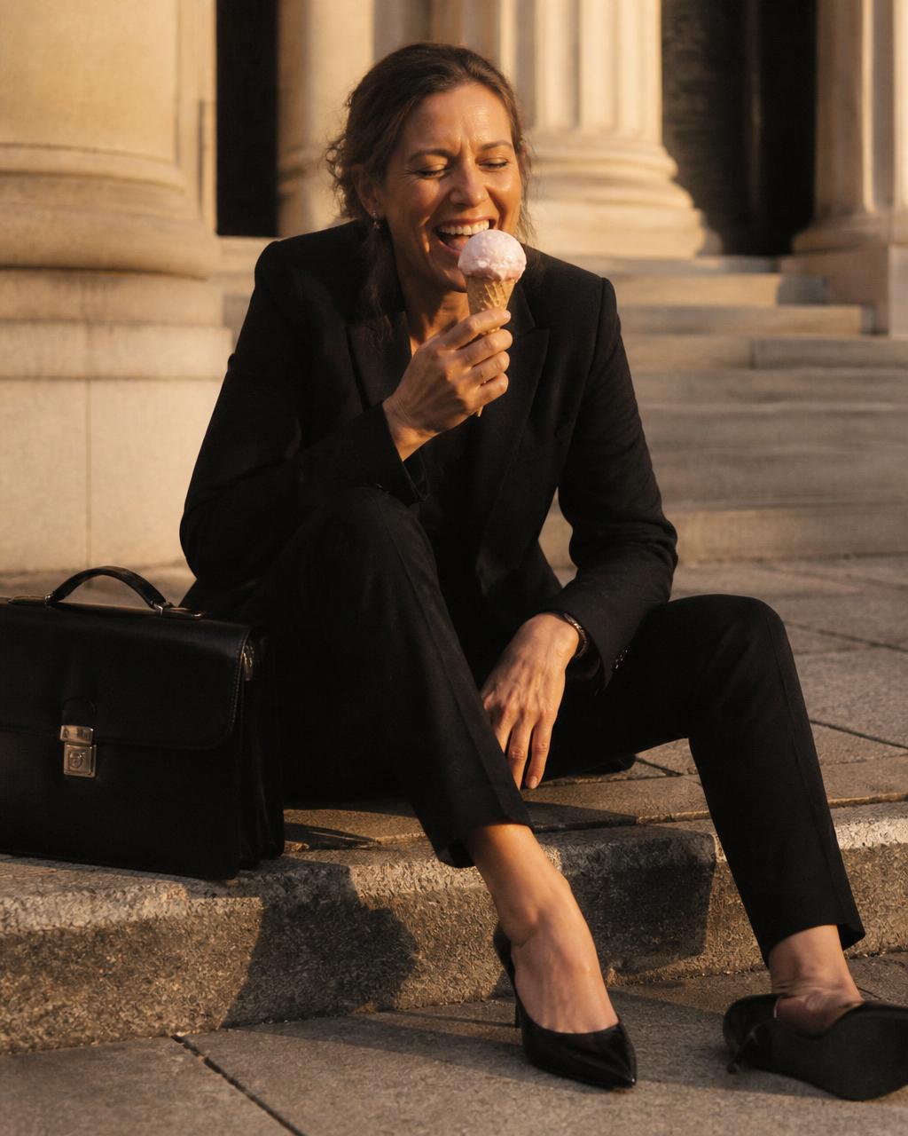 Woman in a black pantsuit eating ice cream on a courthouse curb