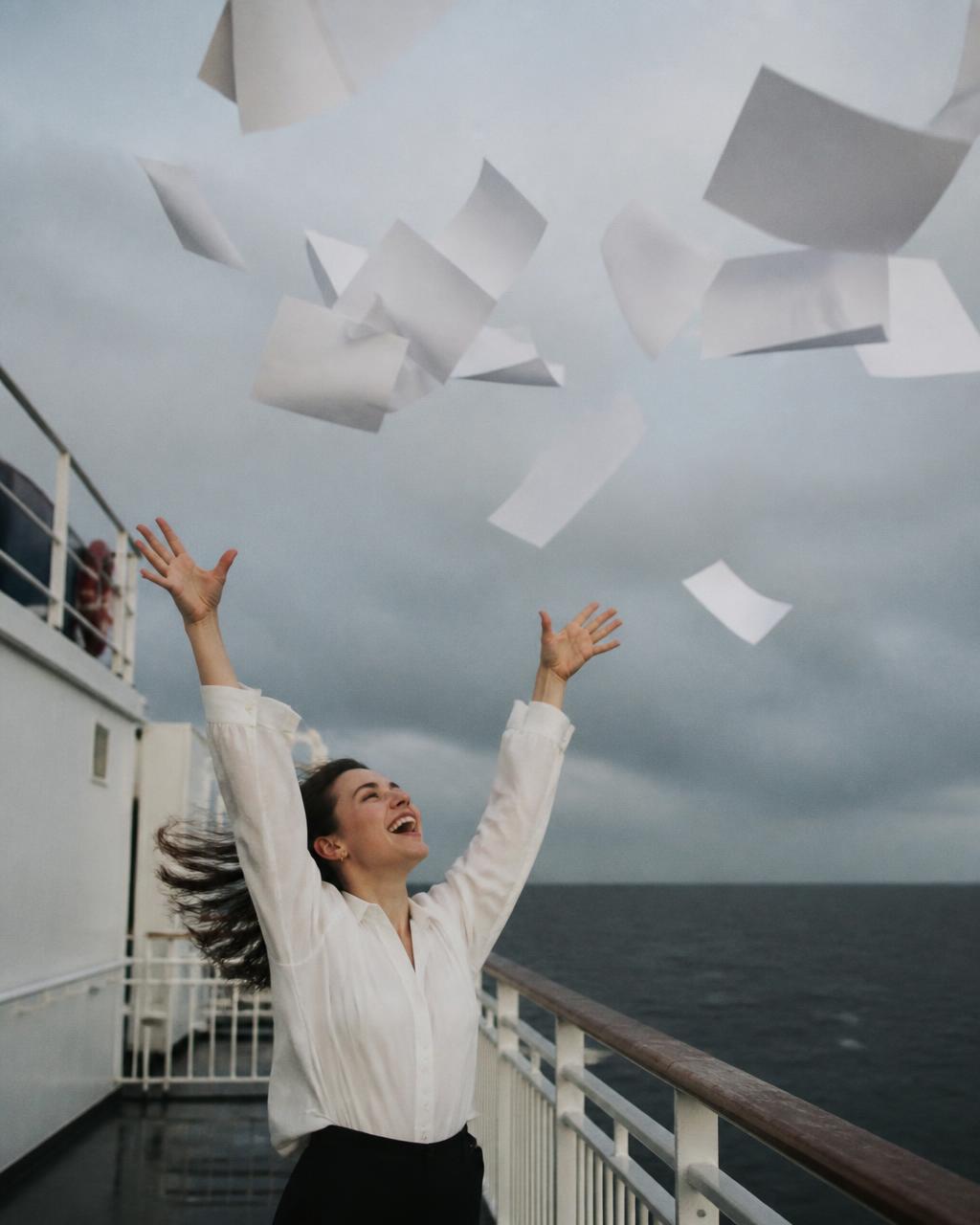 Woman releasing blank papers into the wind from a ferry deck