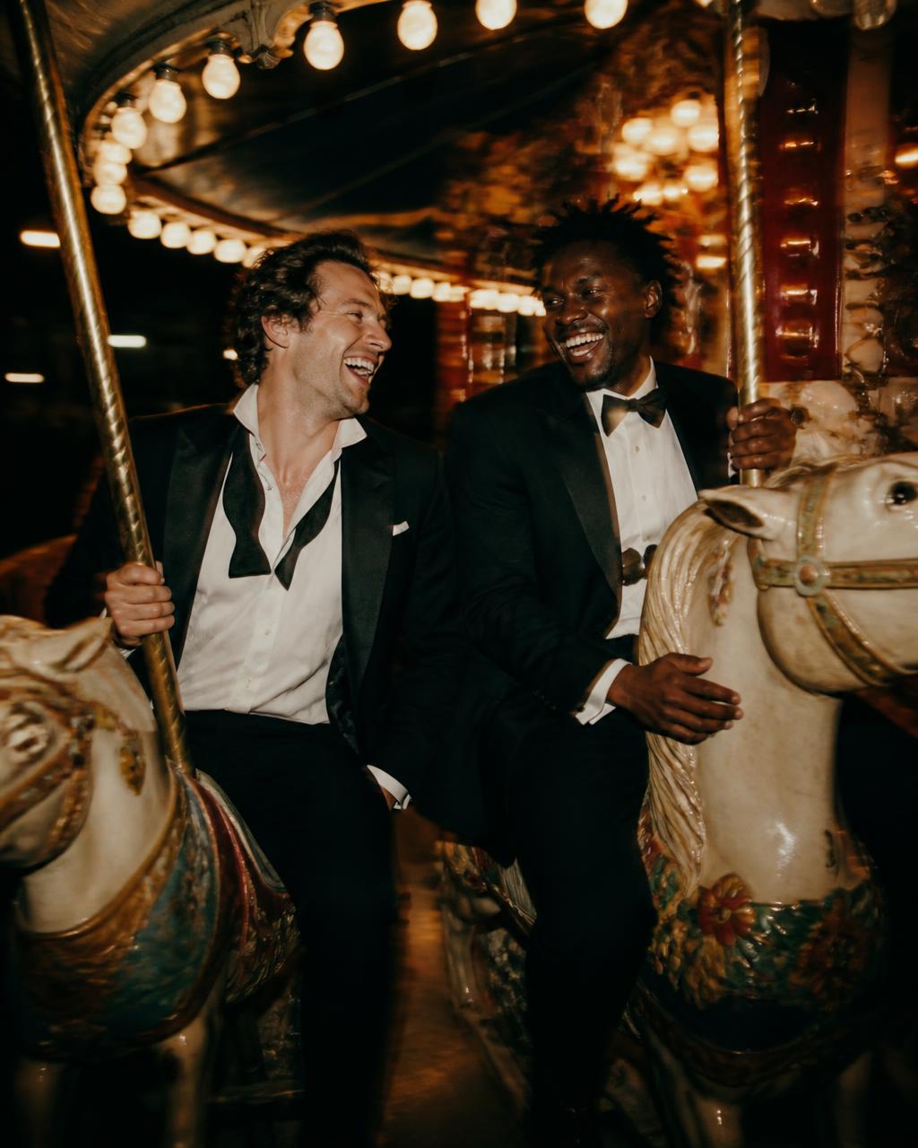 Two men in dinner jackets laughing on a carousel after closing