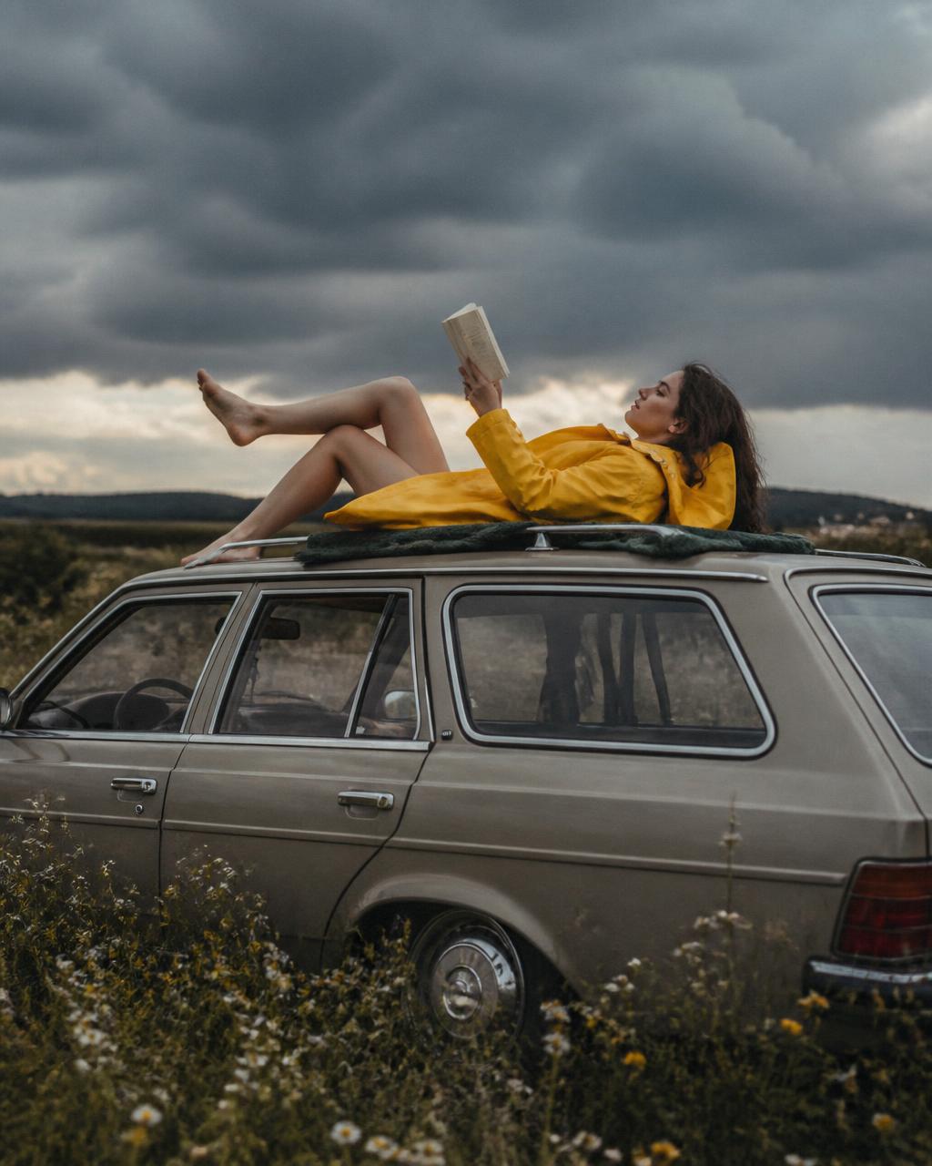 Woman reading on the roof of a station wagon beneath storm clouds