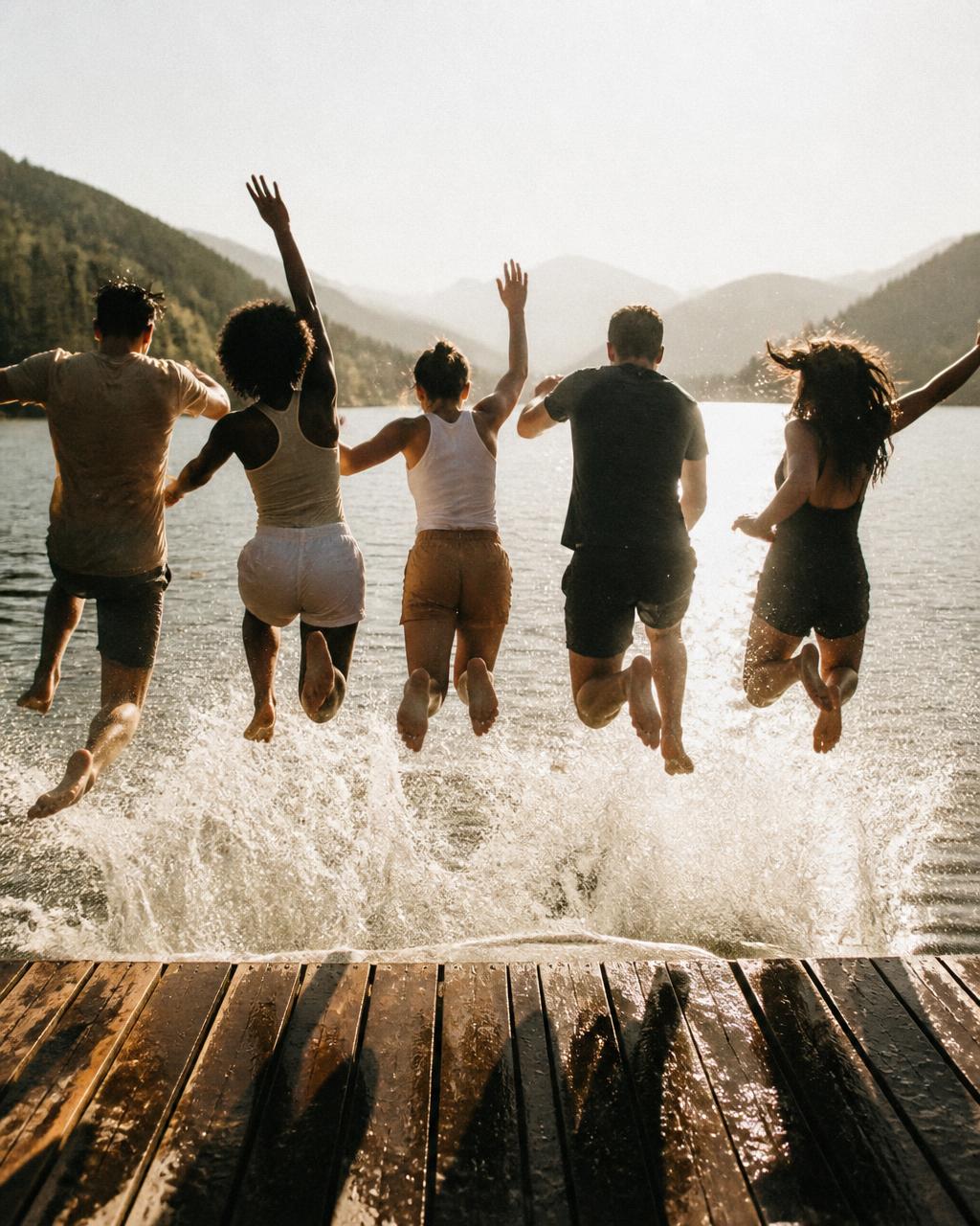 Friends jumping together from a dock into a sunlit lake