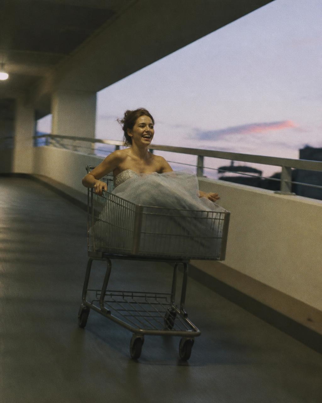 Woman wrapped in towels riding in a shopping cart on a high-rise balcony