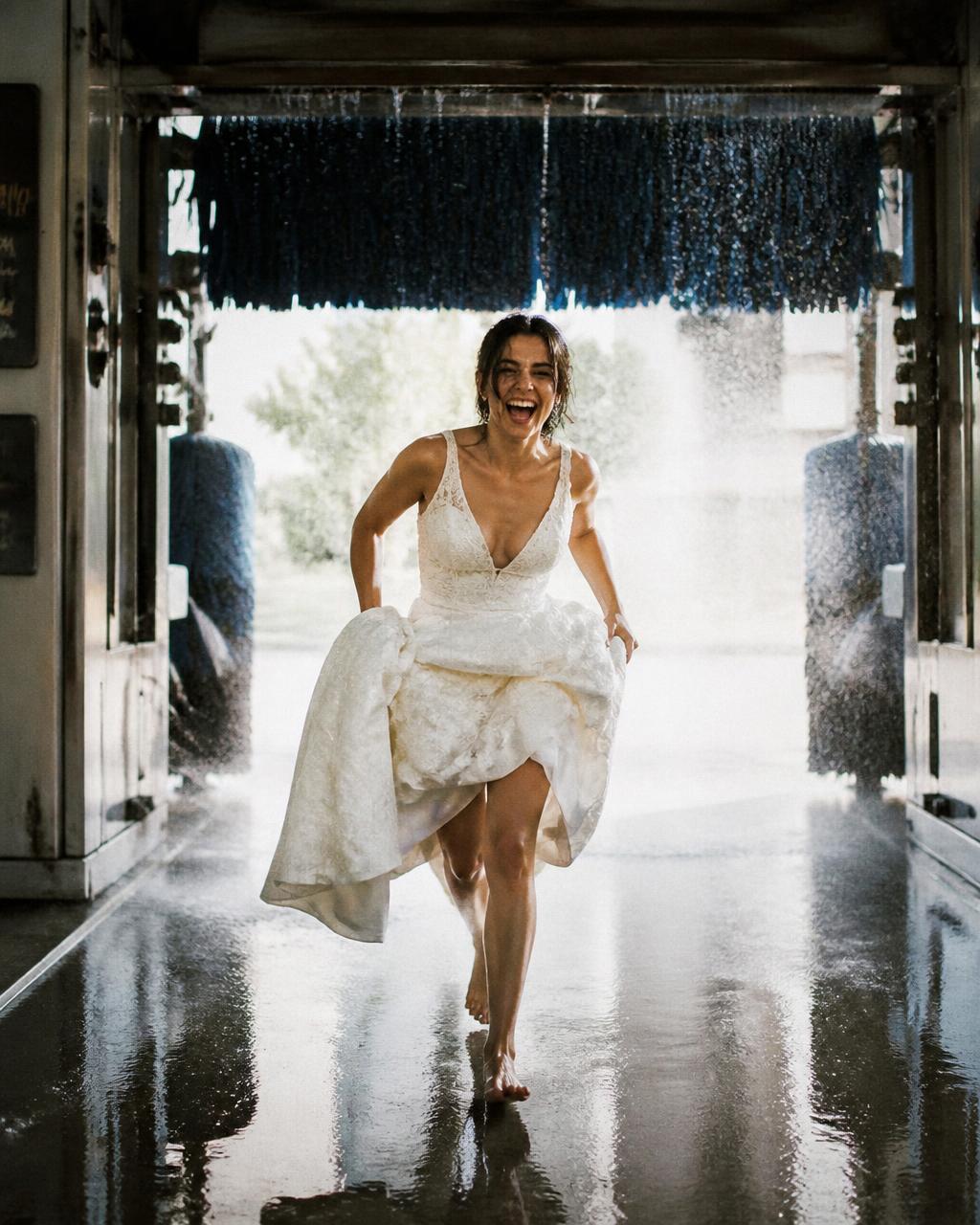 Bride laughing as she runs through a car wash holding her dress