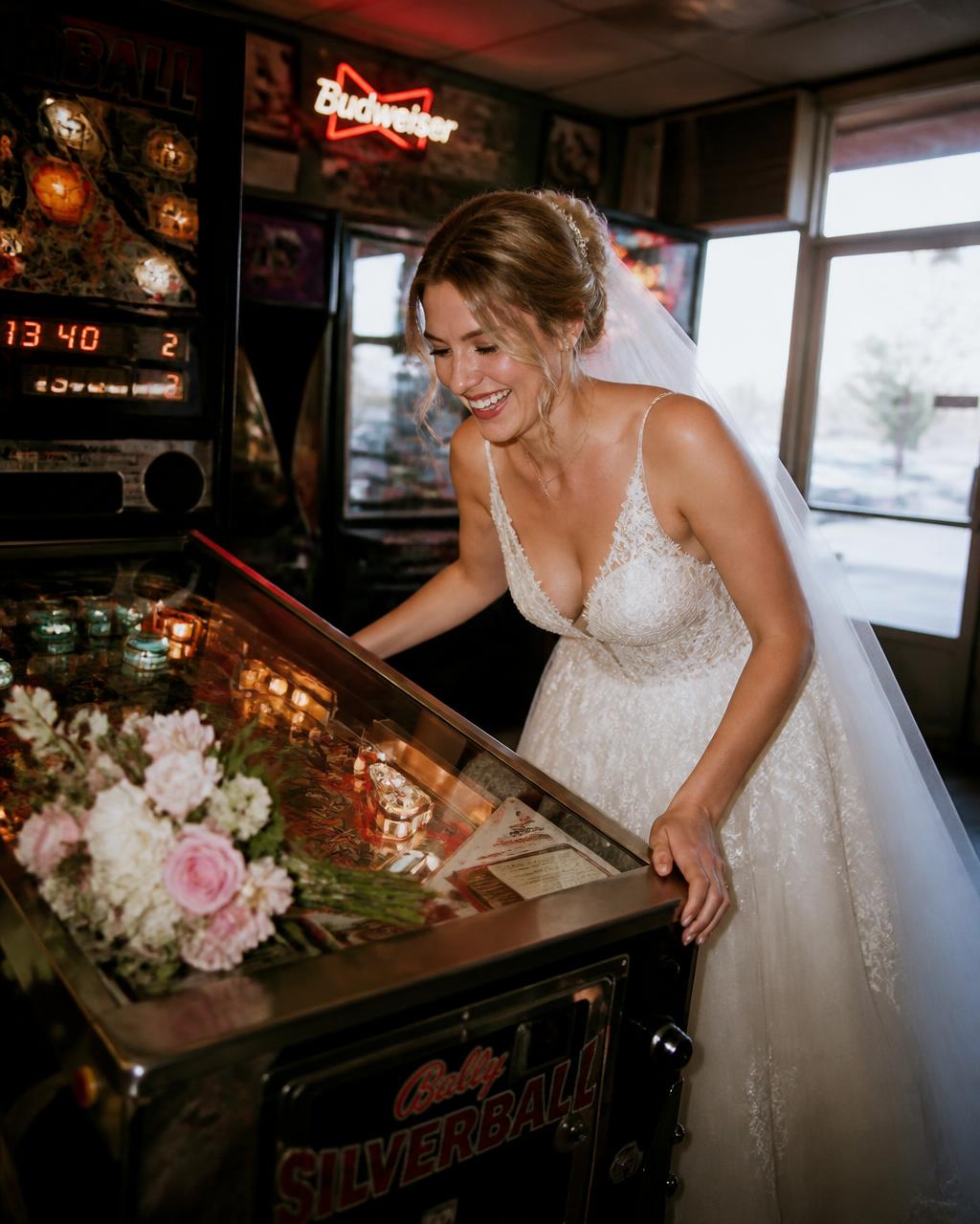 Bride playing pinball in a diner, bouquet resting on the glass