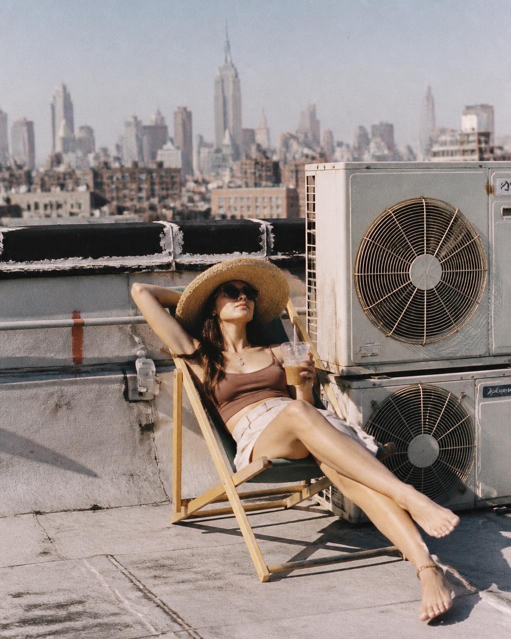 Woman in a sun hat reading in a deck chair beside rooftop air conditioners