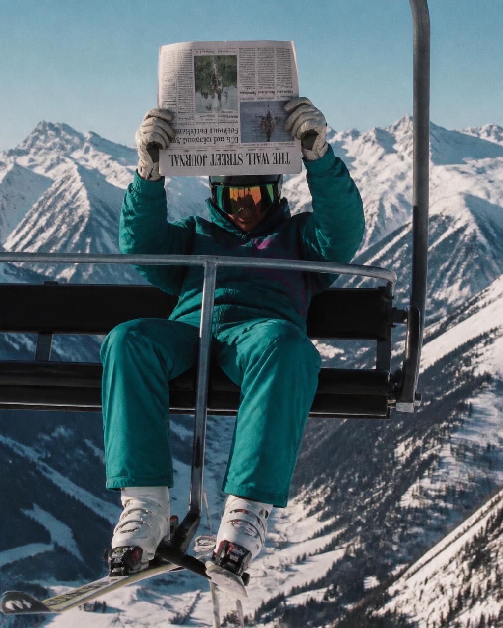 Skier reading the newspaper on a chairlift above snowy peaks