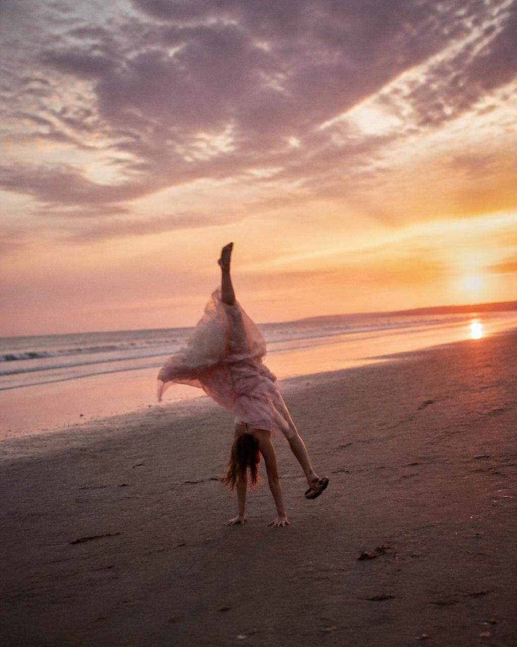 Woman doing a cartwheel on an empty beach at sunset