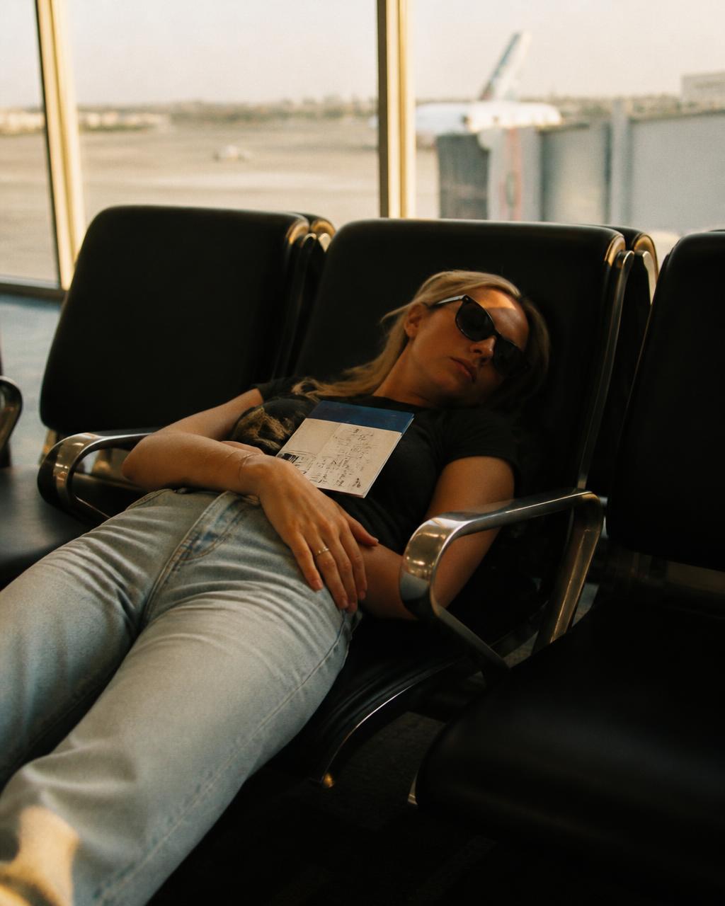 Woman asleep across airport seats with a book on her chest