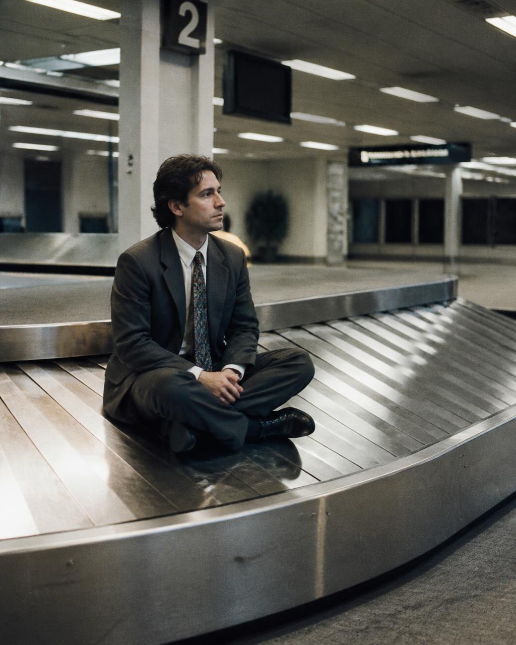 Man in a suit sitting cross-legged on an airport baggage carousel