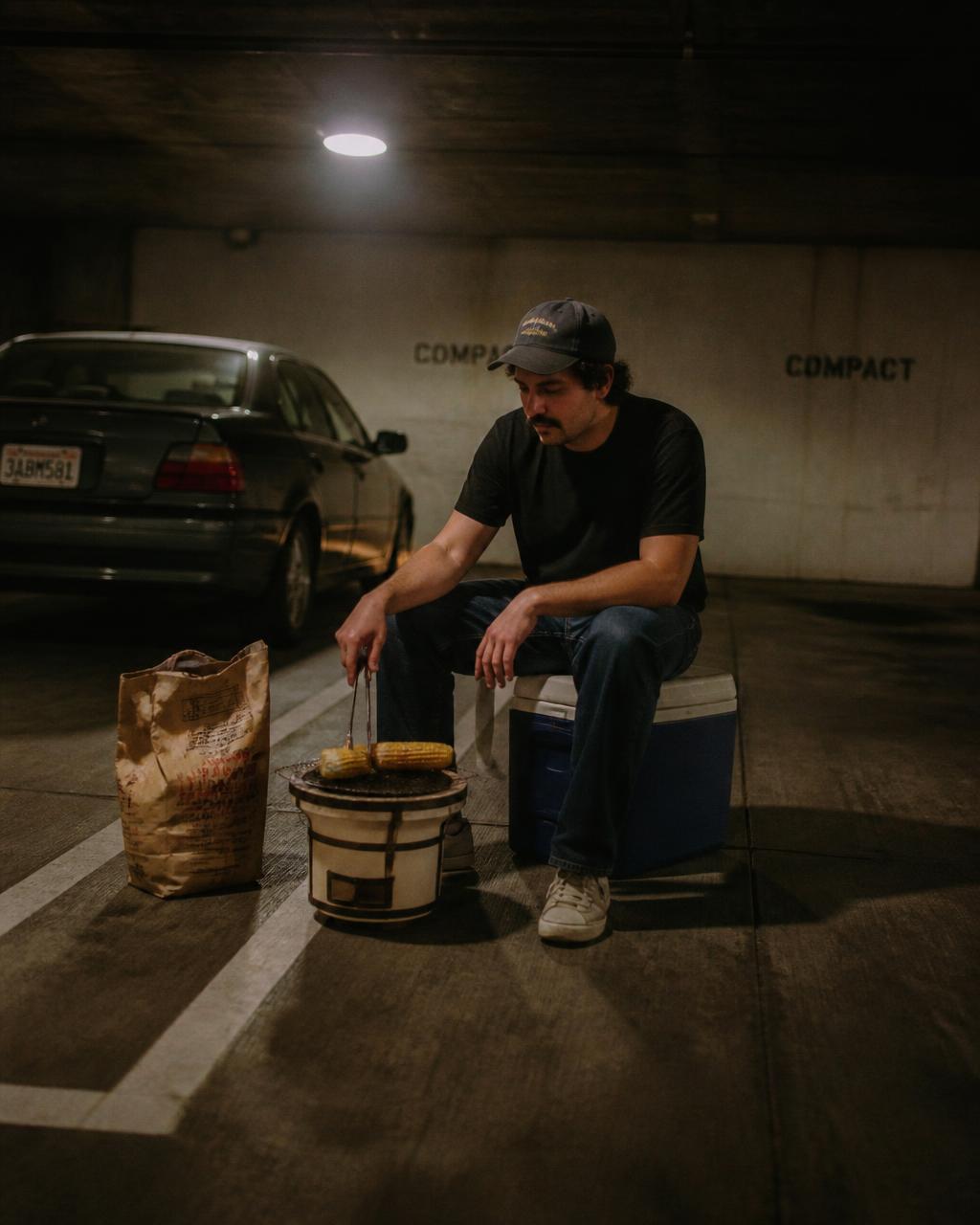 Man grilling on a small hibachi beside his car in a parking garage