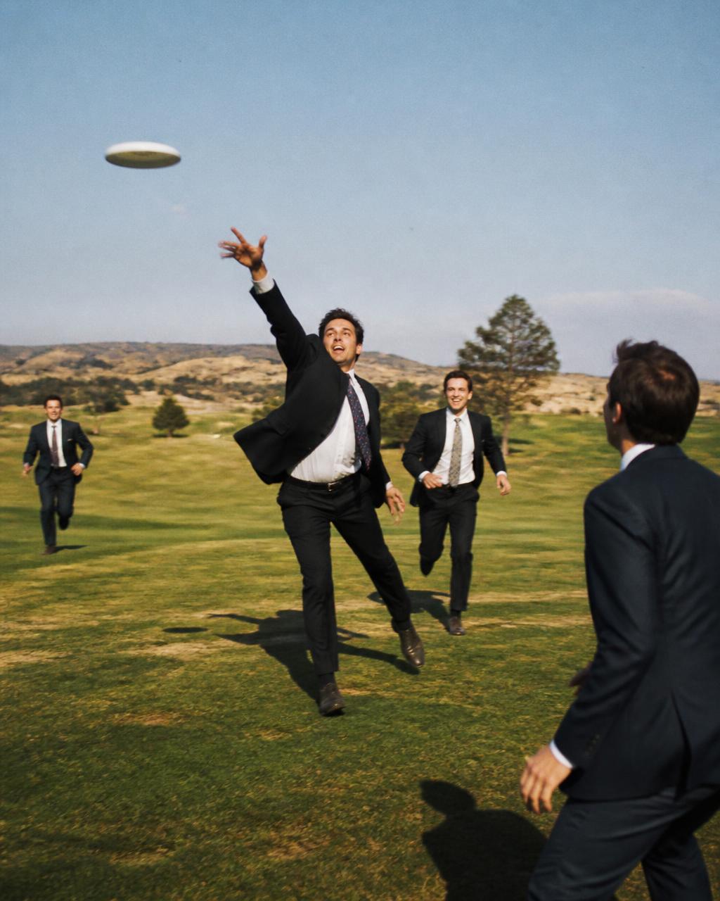Men in suits playing frisbee in a green field