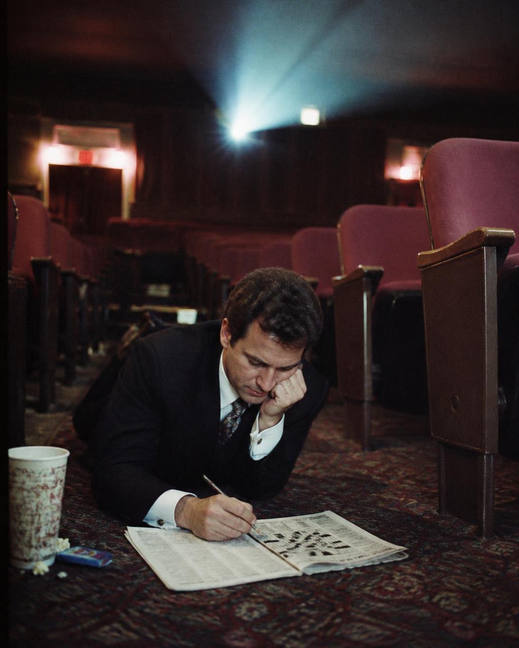 Man in a suit doing a crossword alone in an empty theater