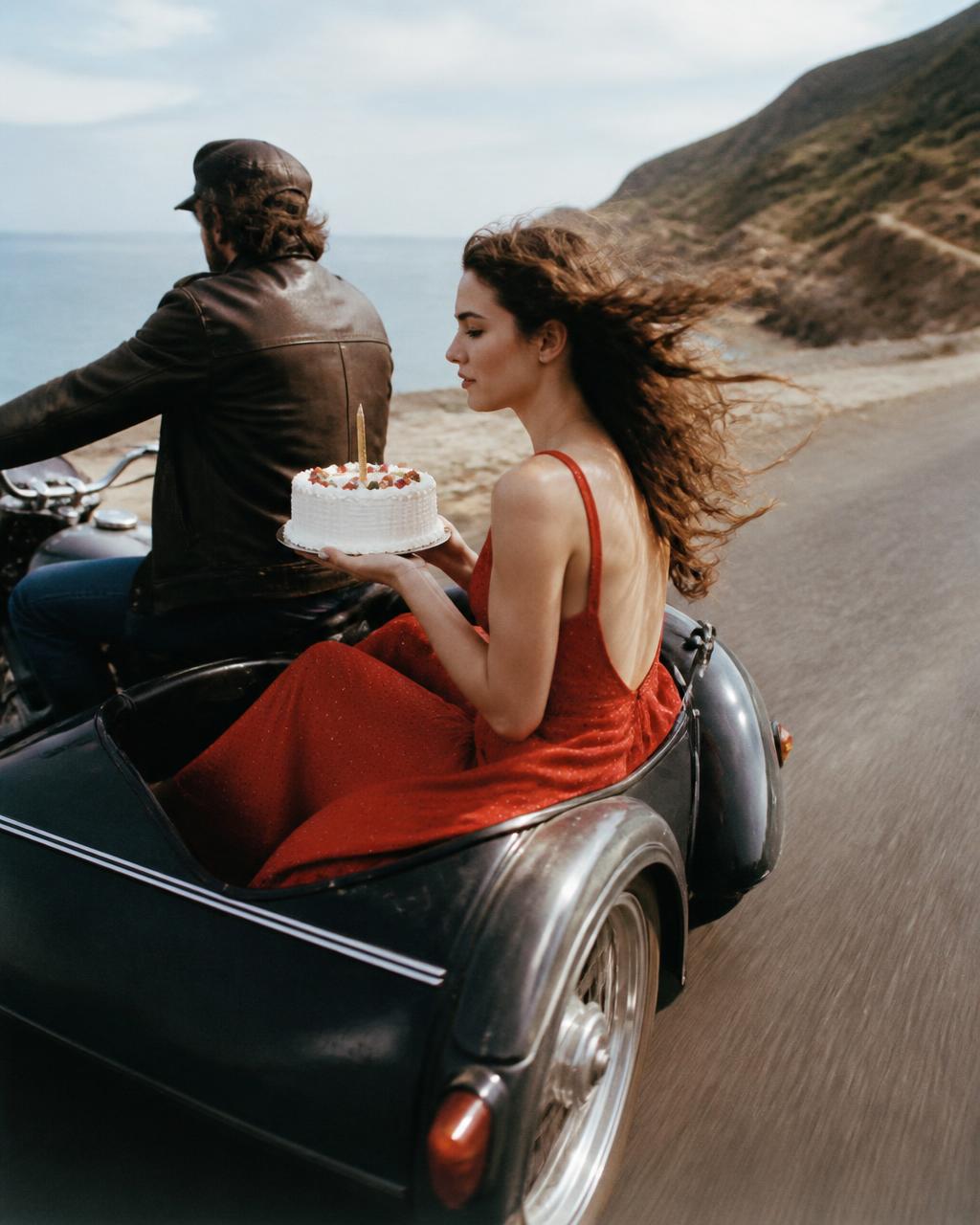 Woman in a red dress holding a cake while riding in a motorcycle sidecar