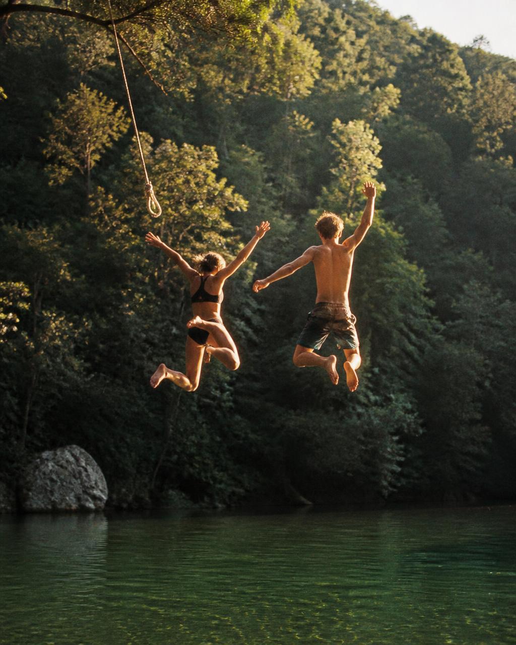 Friends mid-air jumping from a rope swing into a green river