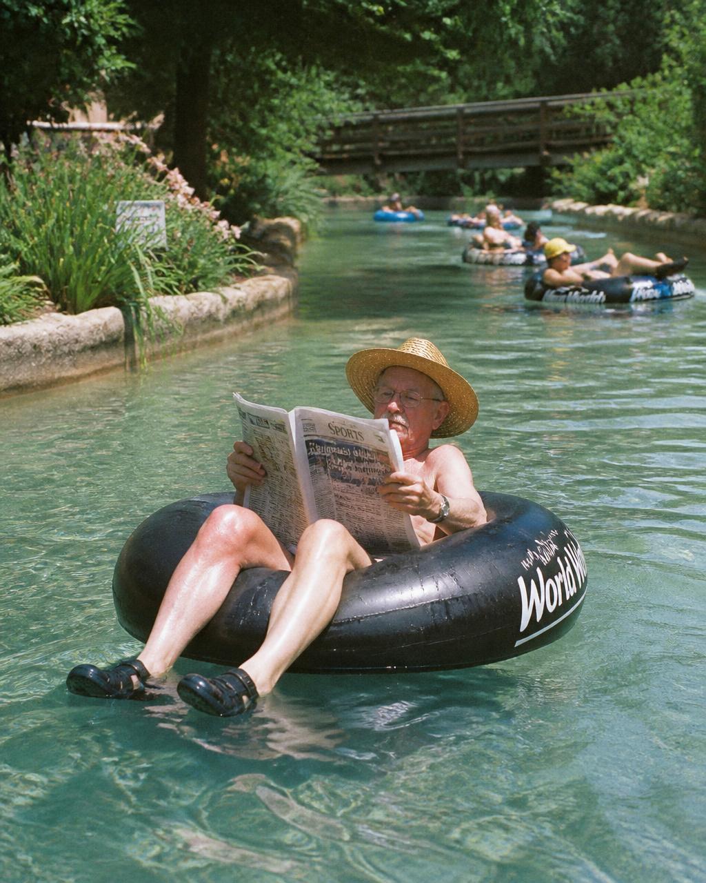 Older man reading the newspaper while floating in an inner tube on a lazy river