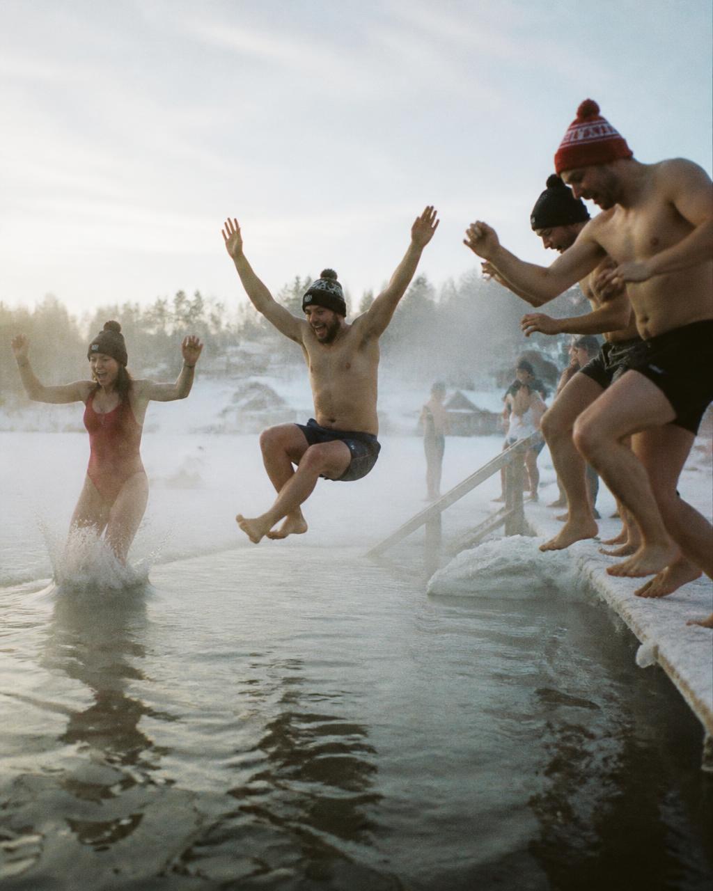 Friends in winter hats leaping into a frozen lake