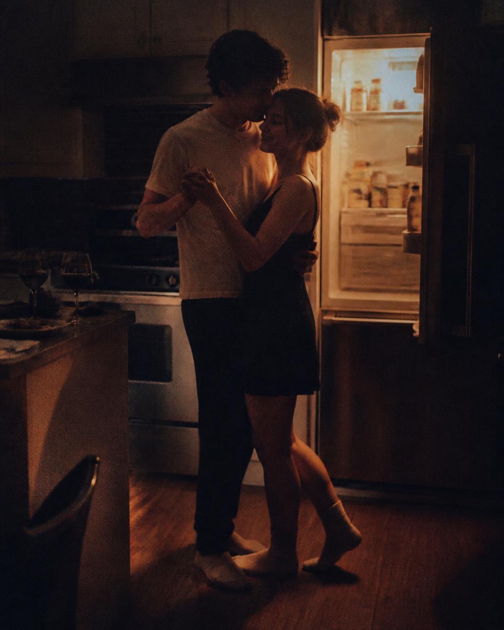 Couple slow dancing in a dark kitchen lit by the fridge