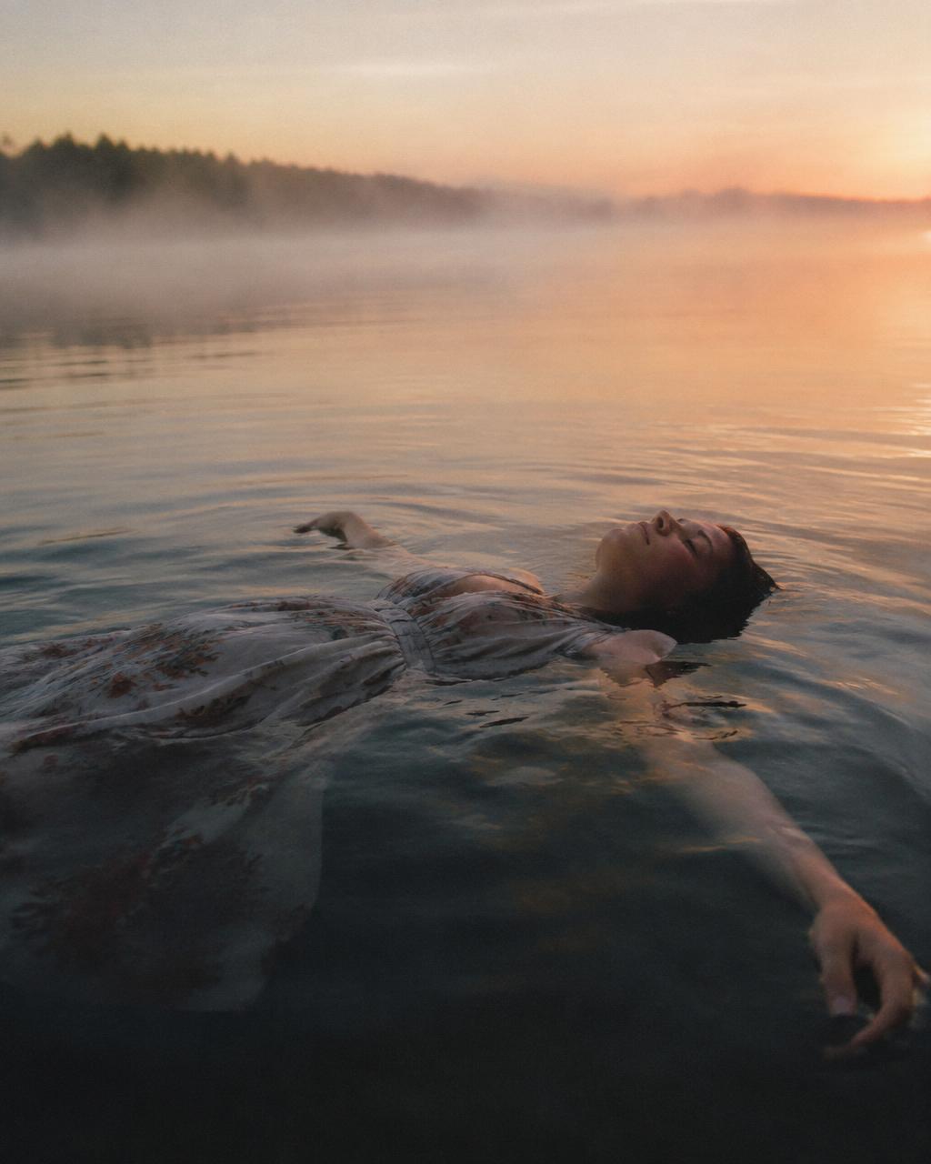 Woman floating on her back in a misty lake at dawn