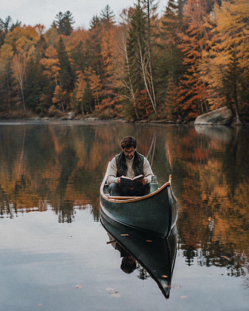 Man reading a book in a canoe on a still autumn pond