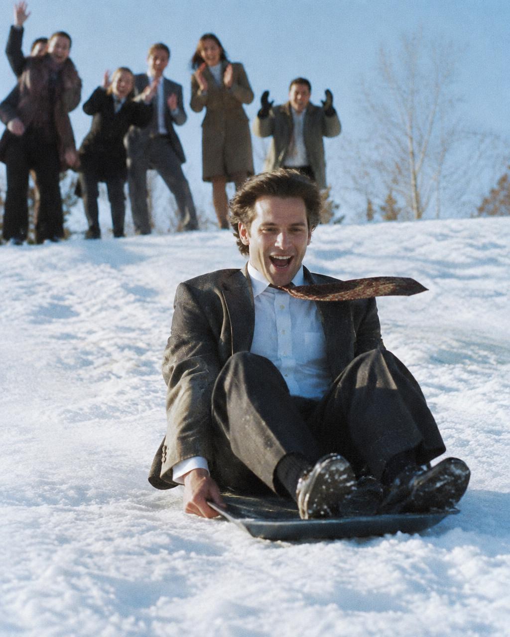 Man in office attire sledding down a hill on a tray