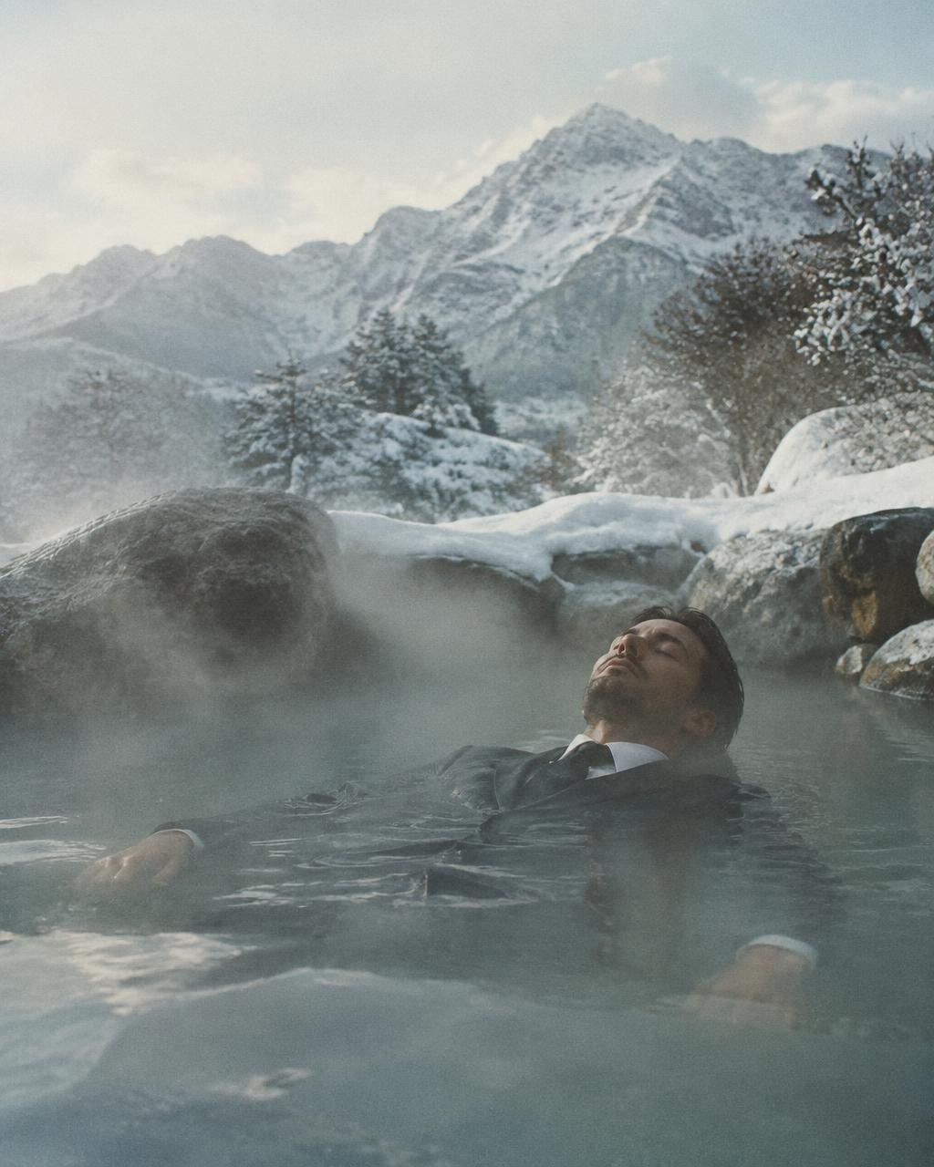 Man in a full suit soaking in a snowy hot spring