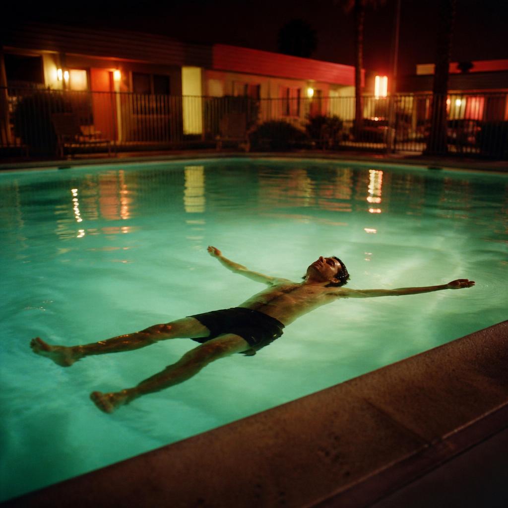 Man floating on his back in a glowing motel pool at night