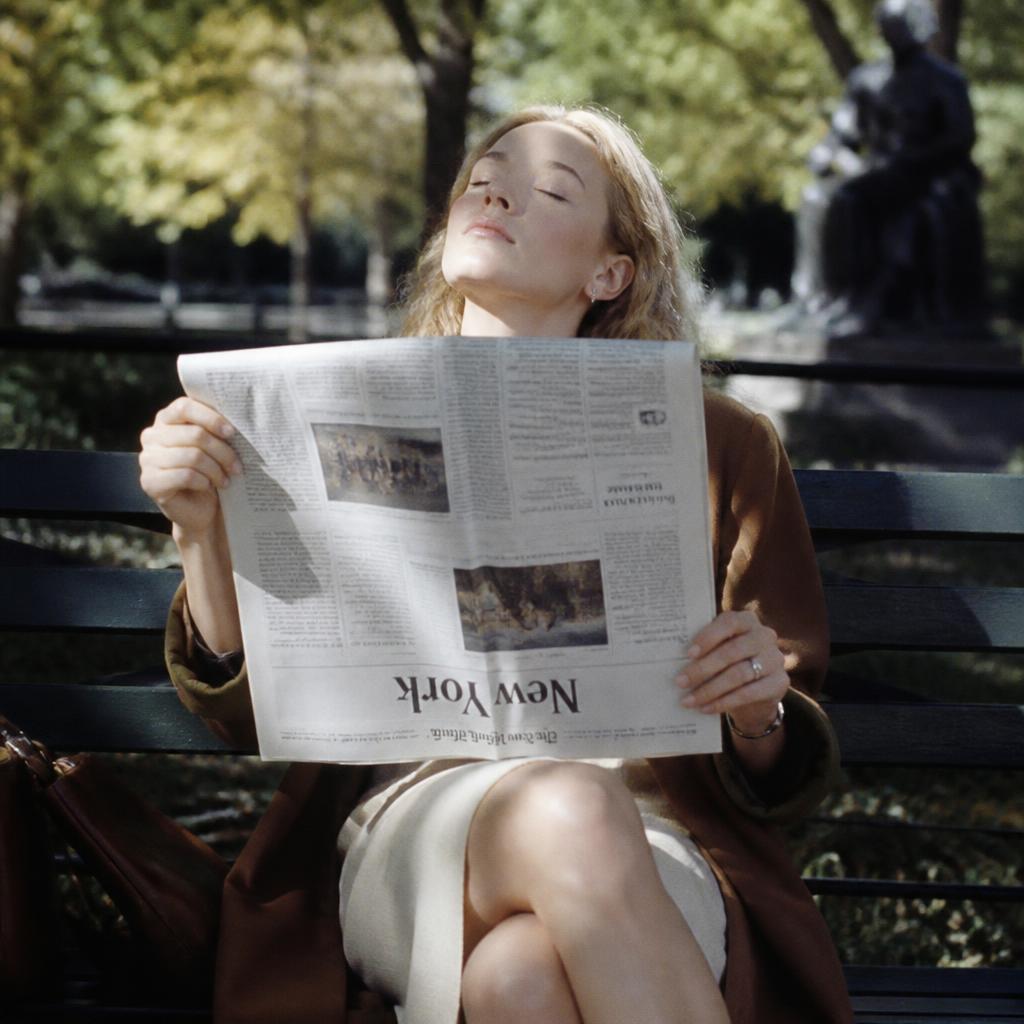 Woman reading a newspaper upside down on a park bench, relaxed